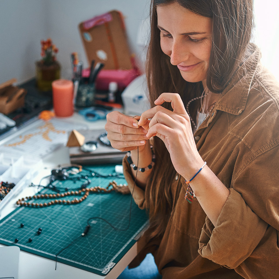 Woman working on beaded jewellery at a desk with jewellery making equipment on it