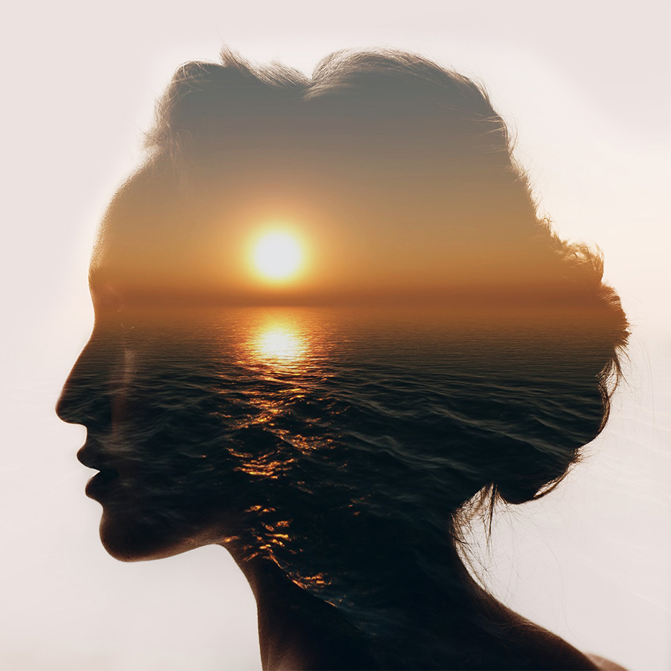 Silhouette of a woman's head, the silhouette is filled with an image of a sunset over an ocean